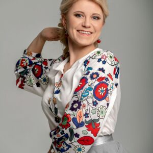 Portrait of a smiling woman wearing a floral embroidered blouse, posing with hand behind head.
